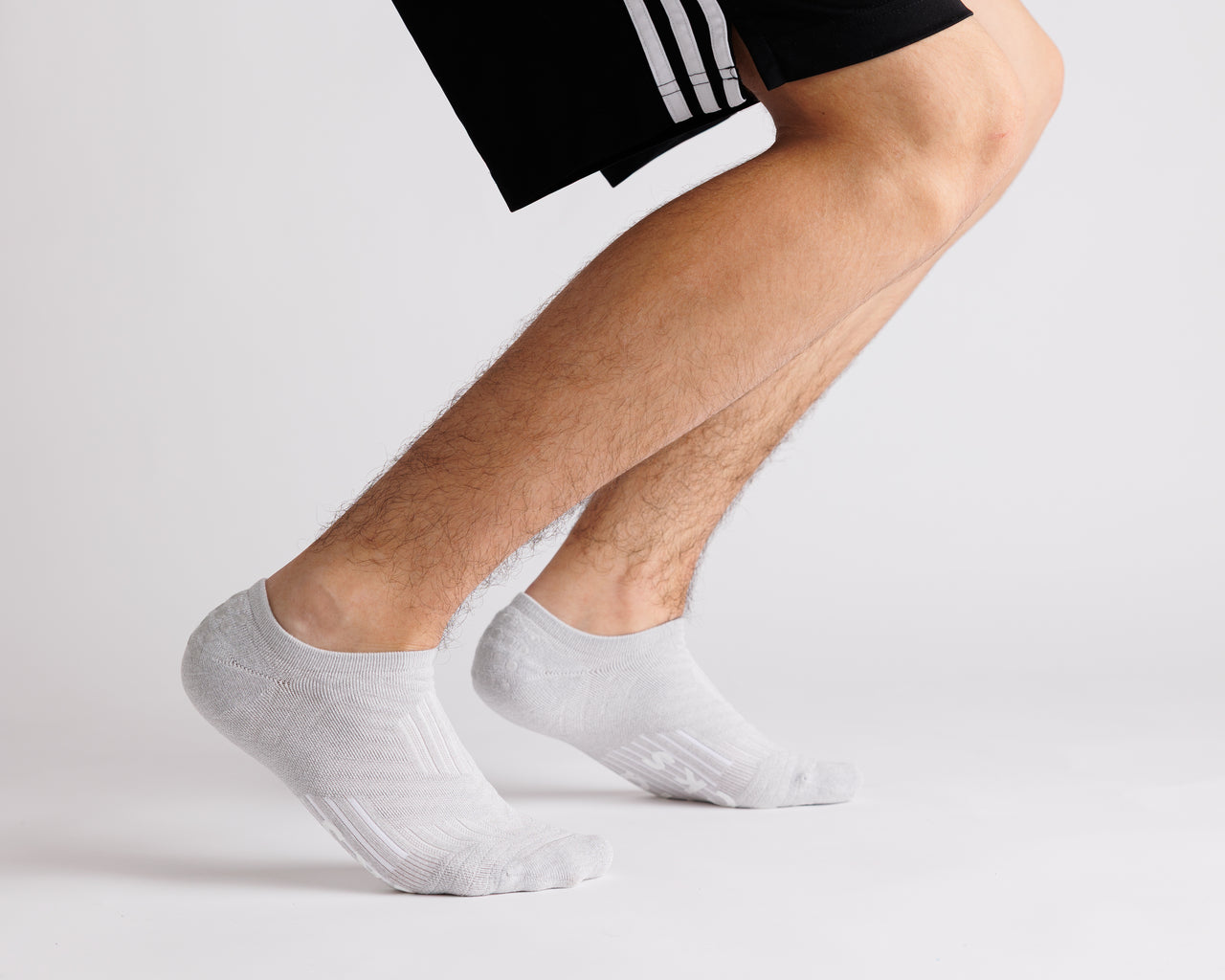 Person wearing gray no-show grip socks with black athletic shorts and heels raised. By Squid Socks.