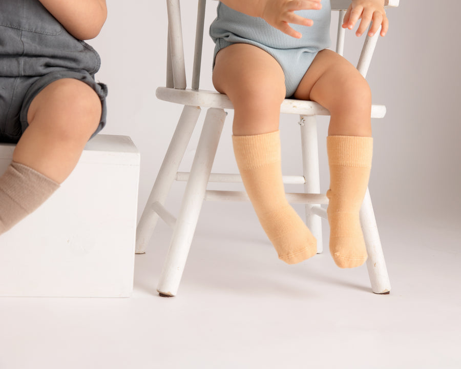 Caramel kids socks: children seated on chairs wearing brown and golden socks. Squid Socks, the brand seen on Shark Tank.