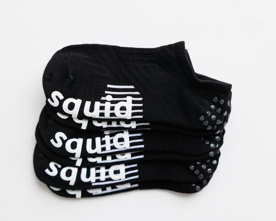 Blackout no-show grip socks stacked with white bottom grips and heel grip dots visible. By Squid Socks.
