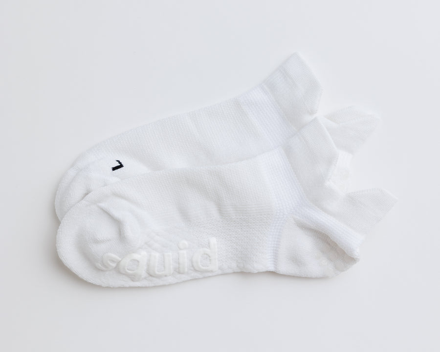 One pair of white ankle grip socks laid together, showing heel tabs and white bottom grips. By Squid Socks.