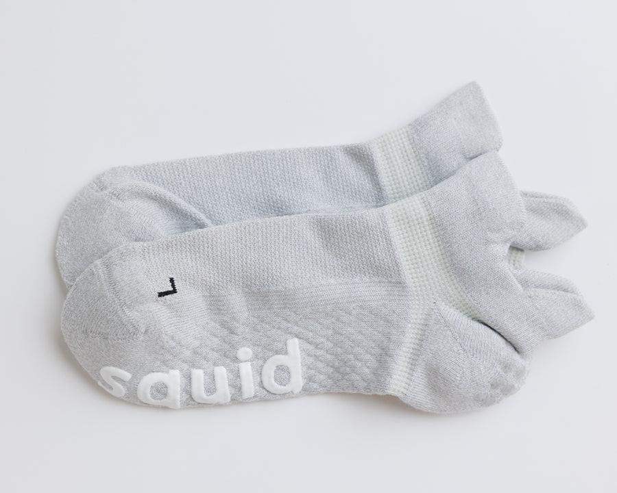 One pair of gray ankle grip socks laid together, showing heel tabs and a left-foot marking. By Squid Socks.
