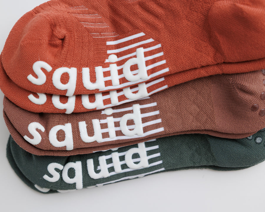 Close-up of stacked terracotta, brown, and muted green no-show socks showing white bottom grips. By Squid Socks.