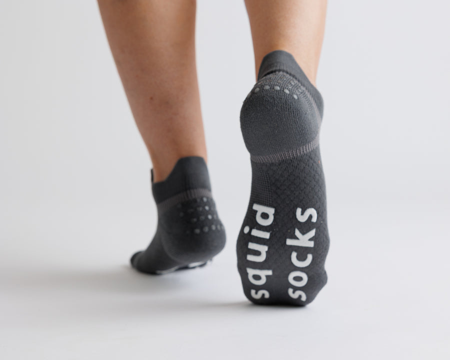 Charcoal gray ankle grip socks with one sole raised to show white bottom grips. By Squid Socks.