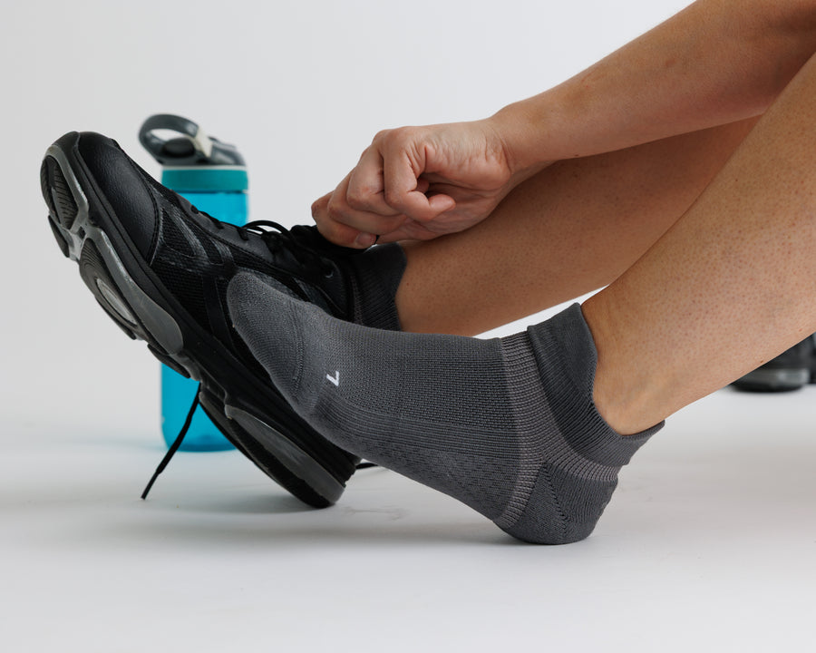 Person wearing charcoal gray ankle grip socks while tying a black athletic shoe. By Squid Socks.