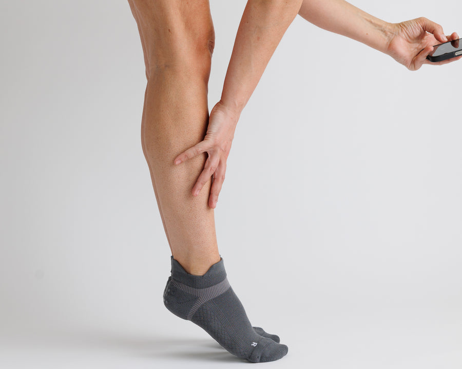 Person stretching while wearing charcoal gray ankle grip socks. By Squid Socks.