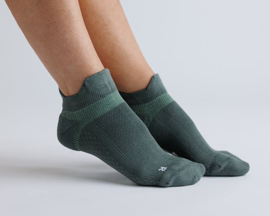 Muted green ankle grip socks worn on both feet, showing side and top views. By Squid Socks.