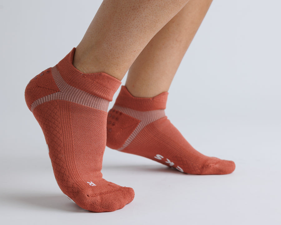 Terracotta ankle grip socks worn with heels raised, showing contrasting knit panels. By Squid Socks.