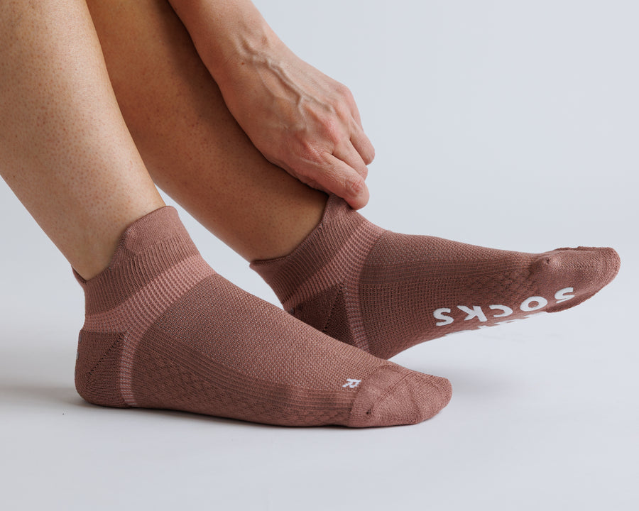Person adjusting a brown ankle grip sock, with white bottom grips visible. By Squid Socks.