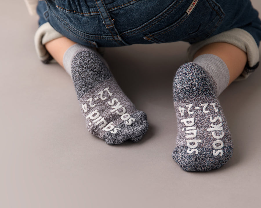 Caelan cotton crew socks: child seated with gray sock soles facing forward. Squid Socks, the brand seen on Shark Tank.