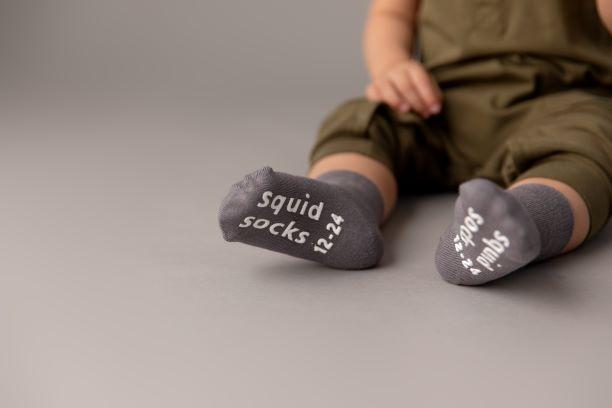Classic kids socks: child seated showing dark gray sole grips. Squid Socks, the brand seen on Shark Tank.