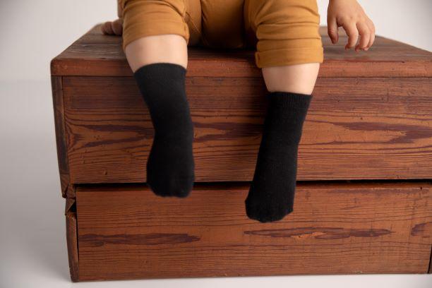 Coal kids socks: child seated with black socks dangling from a wooden box. Squid Socks, the brand seen on Shark Tank.