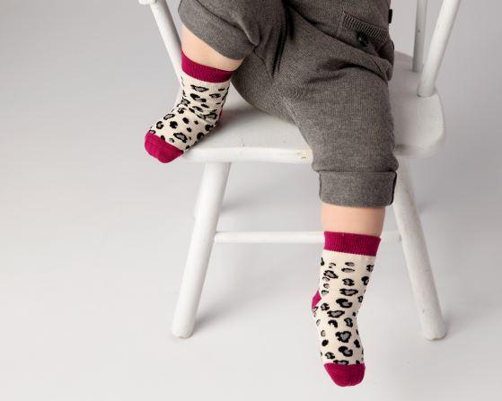 Chanel kids socks: child seated on a chair wearing magenta-cuff leopard socks. Squid Socks, the brand seen on Shark Tank.