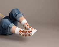 Chesney kids socks: child lying down in white and brown argyle socks. Squid Socks, the brand seen on Shark Tank.