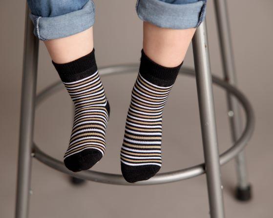 Chesney kids socks: child seated on a stool wearing black striped socks. Squid Socks, the brand seen on Shark Tank.