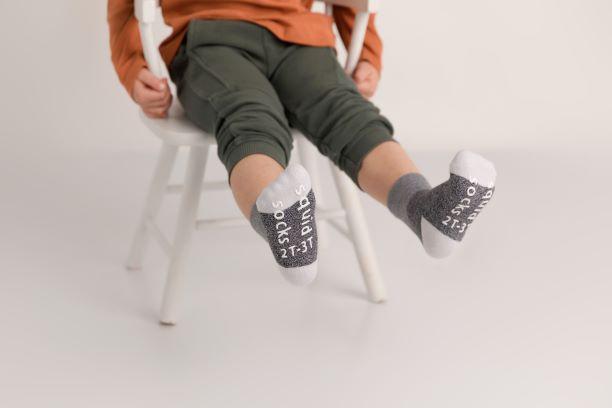 Caelan cotton crew socks: child seated on a chair showing gray sock soles. Squid Socks, the brand seen on Shark Tank.