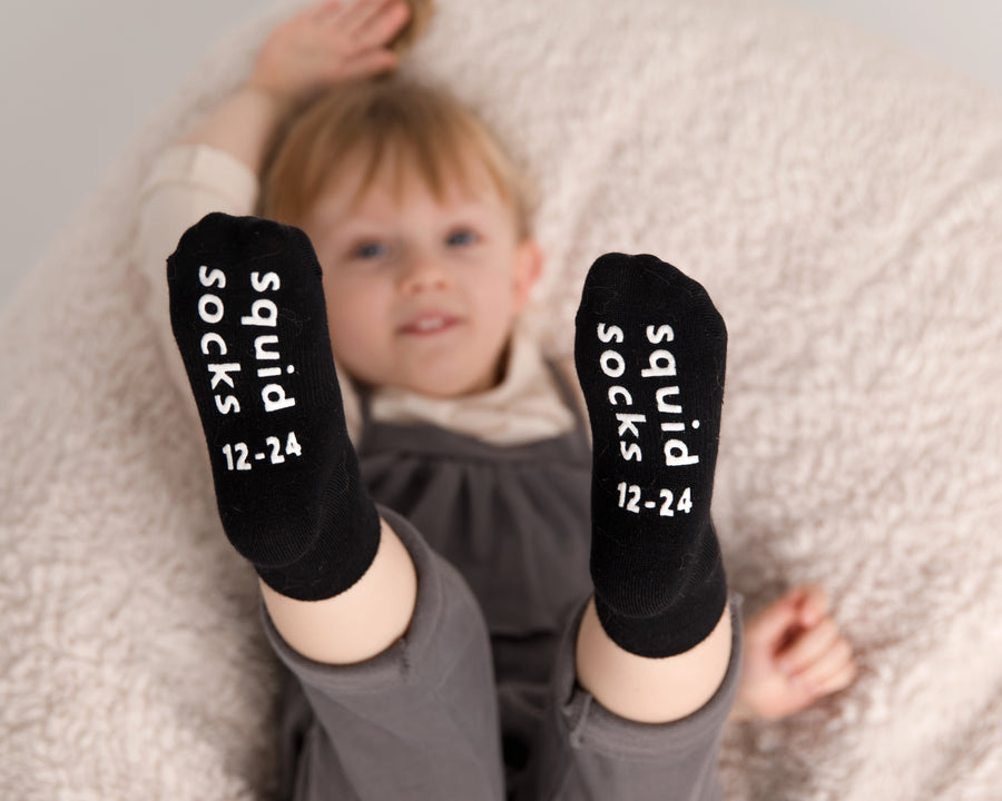 Coal kids socks: child lying on a blanket showing black sock soles. Squid Socks, the brand seen on Shark Tank.