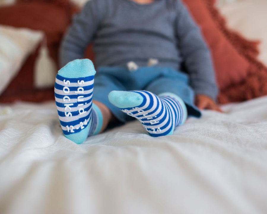 Cruz kids socks: child seated showing blue striped sole grips. Squid Socks, the brand seen on Shark Tank.