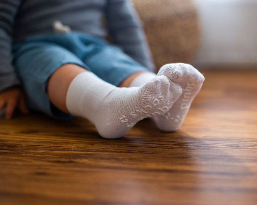 Cloud kids socks: child seated on a wooden floor wearing white socks. Squid Socks, the brand seen on Shark Tank.