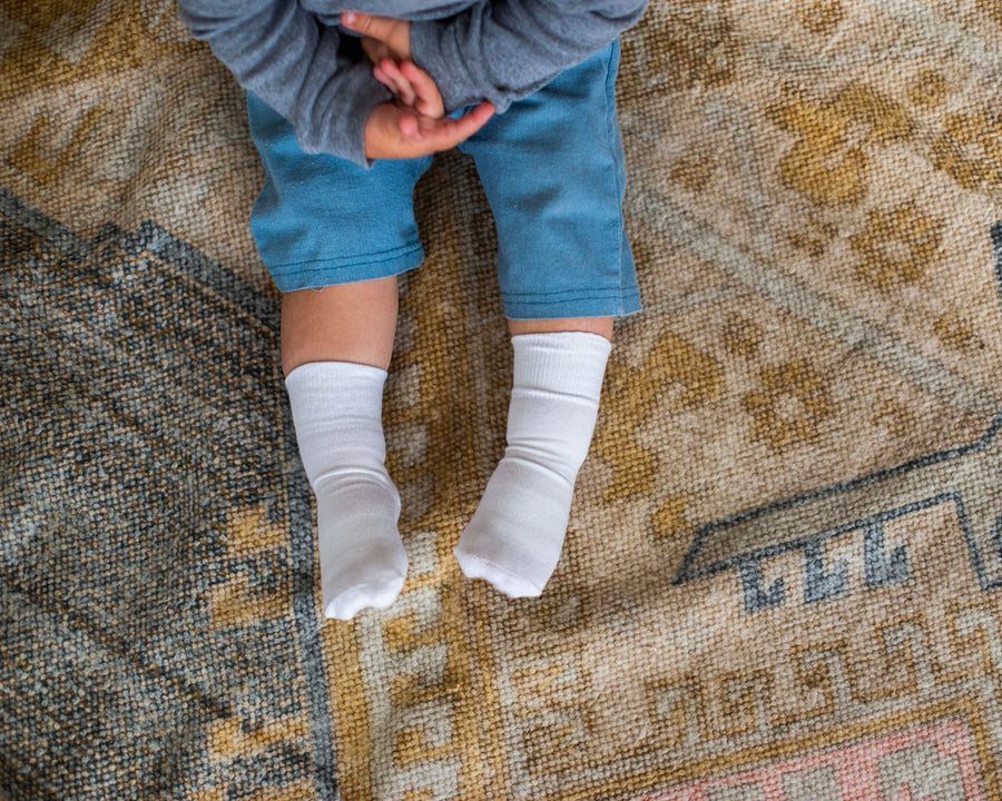 Cloud kids socks: child wearing white socks on a patterned rug. Squid Socks, the brand seen on Shark Tank.