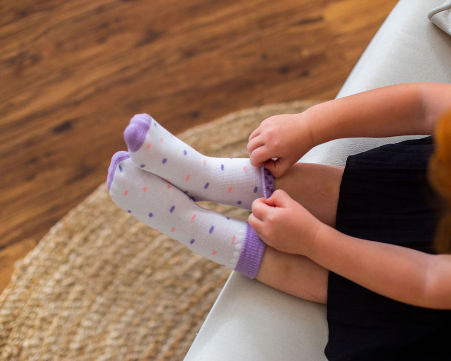 Caroline kids socks: child adjusting white dotted socks while seated. Squid Socks, the brand seen on Shark Tank.
