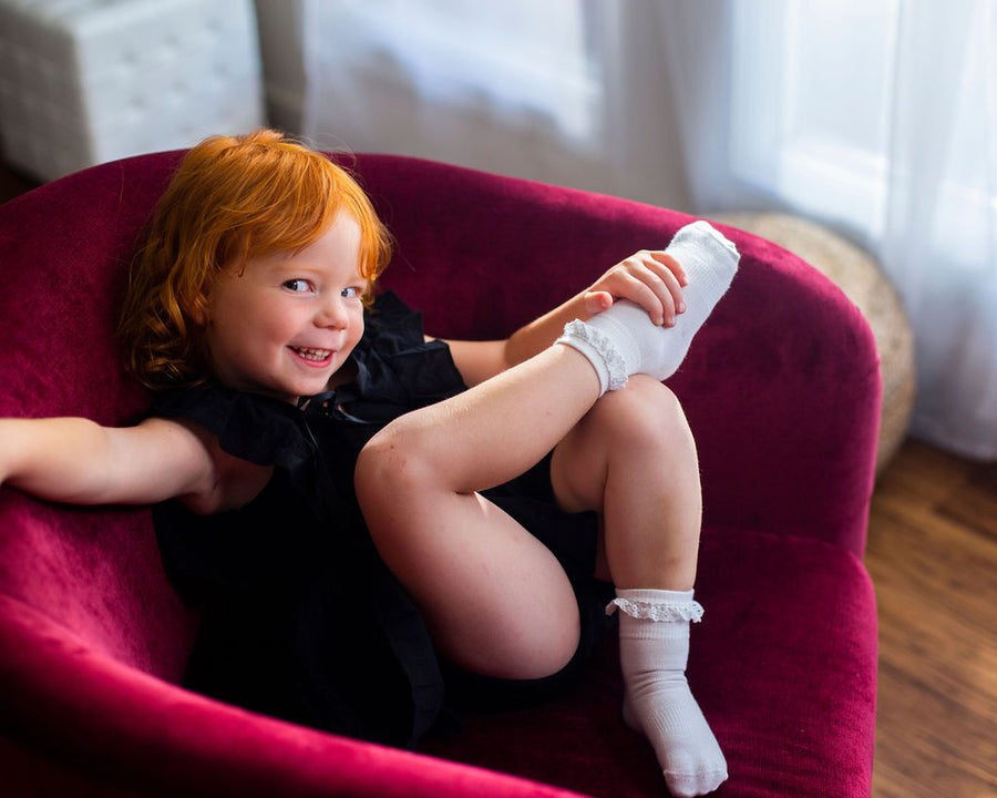 Comfort kids socks: child seated holding a foot in a white lace-trim sock. Squid Socks, the brand seen on Shark Tank.